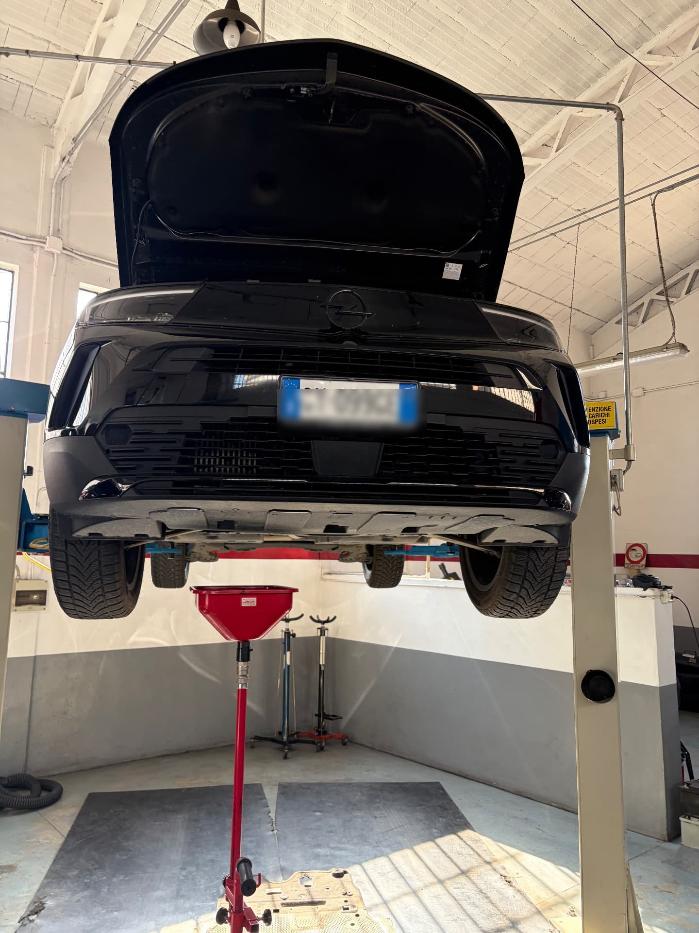 Tagliando in lavorazione su un SUV Opel sollevato sul ponte con raccolta olio